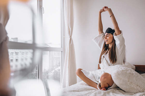Woman in bed wearing sleeping mask and stretching having just woke up